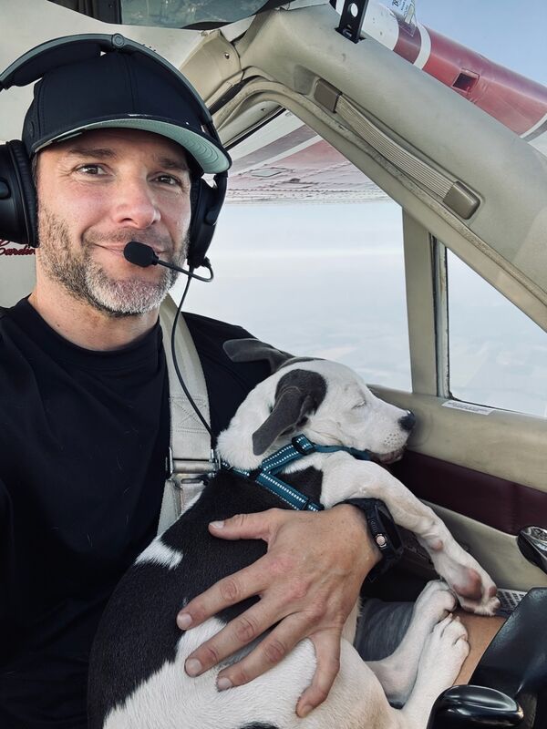Puppy sleeping in pilot's arms mid-flight