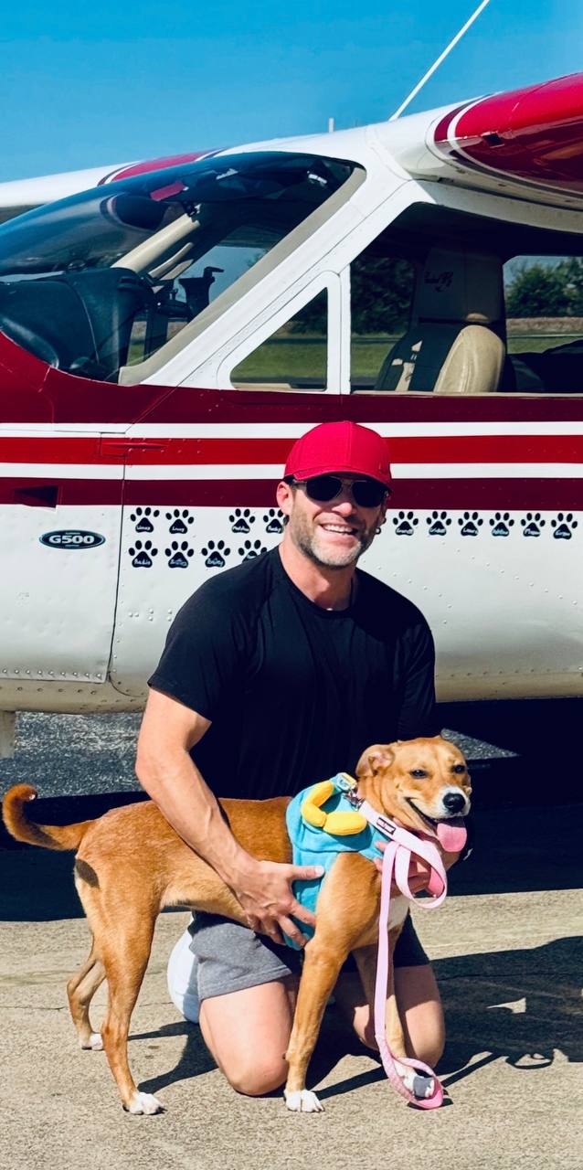 Ryan in a red Hope Wins cap with a rescue dog in front of Hope
